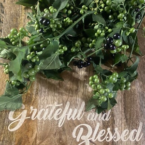 May include: Green and black berries with green leaves on a wooden surface. The words "grateful and blessed" are printed in white script on the wood.