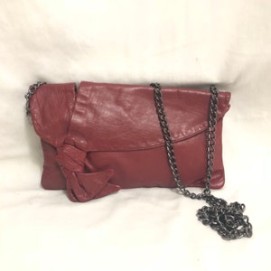 May include: A burgundy leather clutch bag with a chain strap and a large bow detail.