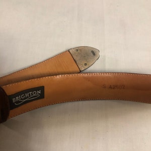 以下が含まれることがあります： 茶色の革製のベルト。銀色のバックルが付いており、ベルトの裏側に「BRIGHTON」と「S 42507」の文字が刻まれています。