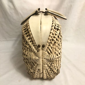 Puede incluir: Un bolso de mimbre blanco con una parte superior de cuero blanco y dos asas negras. El bolso est&aacute; cerrado y tiene un patr&oacute;n tejido.