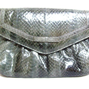 May include: A gray snakeskin clutch purse with a flap closure and a gold chain strap.