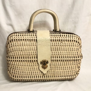 Puede incluir: Un bolso de mimbre blanco con asa de cuero y cierre met&aacute;lico decorativo. El bolso tiene un dise&ntilde;o tejido y una correa de cuero blanco.