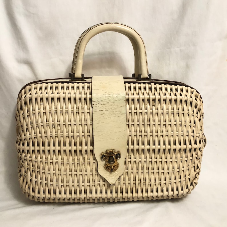 Puede incluir: Un bolso de mimbre blanco con asa de cuero y cierre met&aacute;lico decorativo. El bolso tiene un dise&ntilde;o tejido y una correa de cuero blanco.