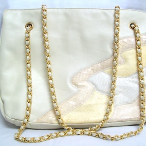 May include: A white leather handbag with a gold chain strap. The bag has a patchwork design with different shades of white and cream leather.