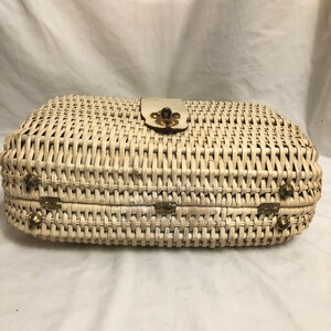 Puede incluir: Un bolso de mimbre blanco tejido con cierre de lat&oacute;n y detalles decorativos. El bolso tiene forma rectangular y un patr&oacute;n tejido.