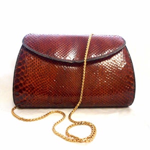 May include: A brown snakeskin clutch purse with a gold chain strap.