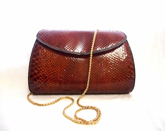 May include: A brown snakeskin clutch purse with a gold chain strap.