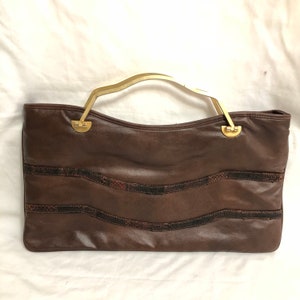 May include: A brown leather handbag with a gold-tone handle and a snakeskin pattern. The bag has a top flap closure and a structured shape.