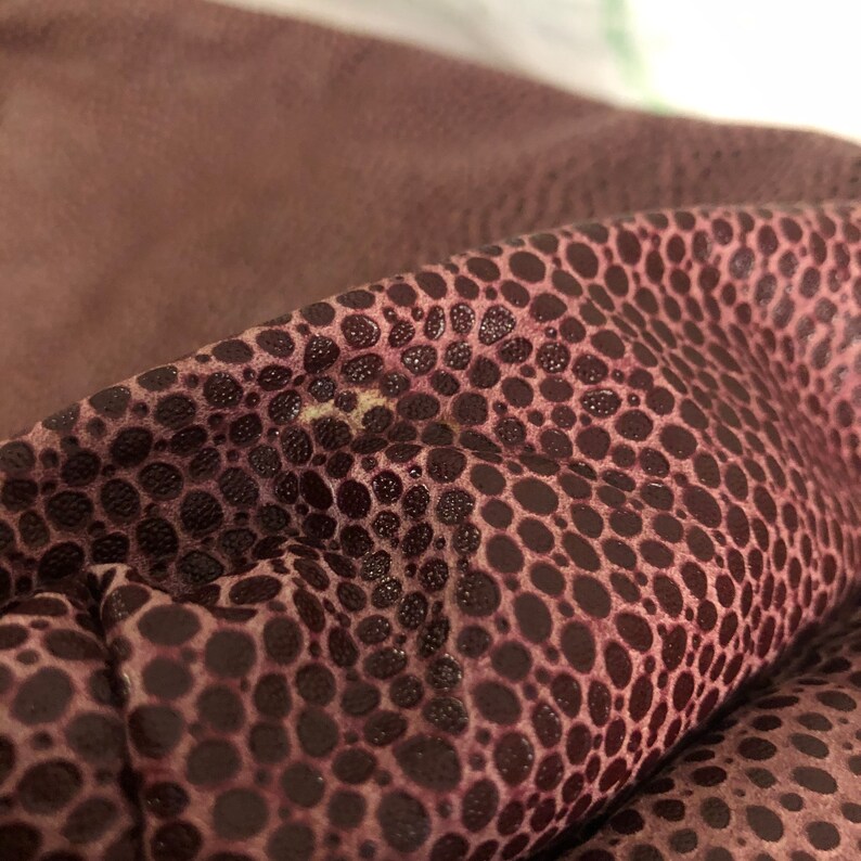 May include: Close-up of a burgundy leather material with a textured pattern of small, dark circles.