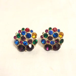 May include: A pair of gold tone clip-on earrings with a cluster of colorful rhinestones. The earrings feature a variety of colors, including red, blue, green, yellow, and purple.
