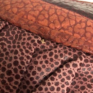 May include: Close-up of a burgundy textured fabric with a repeating pattern of small circles. The fabric has a subtle sheen and a slightly raised texture.