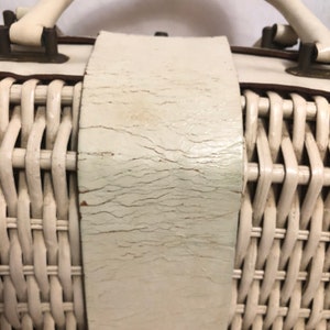 Puede incluir: Bolso de mimbre blanco con una correa y asas de cuero blanco. El cuero tiene un aspecto agrietado y desgastado.