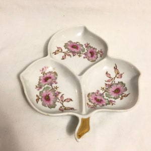 May include: A white porcelain serving dish shaped like a leaf with three sections. The dish is decorated with pink and green floral designs.