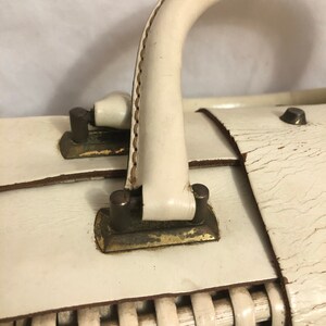 Puede incluir: Maleta vintage de cuero blanco con base de mimbre tejido y herrajes de lat&oacute;n. La maleta tiene un solo asa y un aspecto desgastado y envejecido.