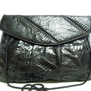 May include: A black leather clutch purse with a snakeskin pattern. The purse has a flap closure and a chain strap.