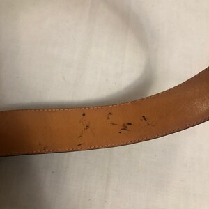 以下が含まれることがあります： 茶色の革製のベルトの裏側のクローズアップ。ベルトには擦り傷や傷があります。