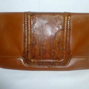 May include: A brown leather clutch with a snakeskin pattern on the front. The clutch has a flap closure and a smooth leather finish.