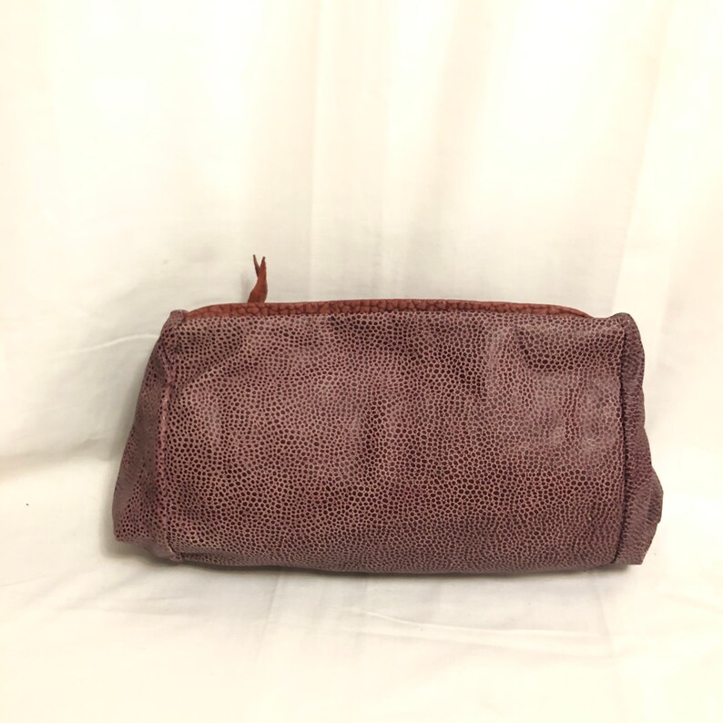 May include: A small, rectangular, burgundy-colored leather clutch bag with a zipper closure.