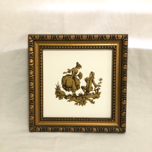 May include: A framed picture with a gold-colored frame and a white background. The picture depicts a couple in a romantic scene, with the man kneeling and the woman standing. The couple is silhouetted in gold.