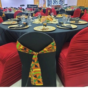 May include: A black tablecloth with gold chargers and red napkins covers a table set for a formal event. Black chairs with red covers and black chairs with colorful fabric sashes are arranged around the table. A sign that reads "Reserved" is placed on the table.