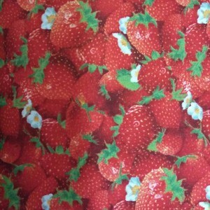 May include: A red fabric with a repeating pattern of strawberries and white flowers. The strawberries are red and green and the flowers are white with a light blue center.