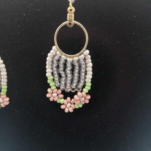 May include: A pair of dangle earrings with a gold hoop and a beaded fringe. The fringe is made of white, clear, and green beads. The bottom of the fringe is decorated with pink flowers.