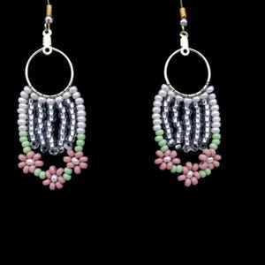 May include: A pair of dangle earrings with a silver and white beaded design. The earrings feature a pink and green flower design at the bottom.