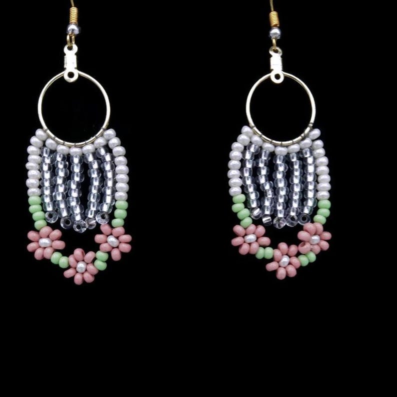 May include: A pair of dangle earrings with a silver and white beaded design. The earrings feature a pink and green flower design at the bottom.