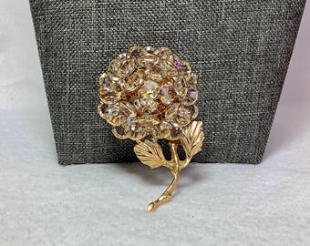 Könnte beinhalten: Eine goldfarbene Brosche in Form einer Rose mit klaren Strasssteinen. Die Rose hat einen Stiel und Blätter.