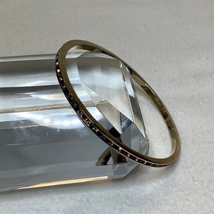 May include: A silver bangle bracelet with a row of small red and clear rhinestones around the edge.
