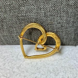 May include: Gold-toned heart-shaped brooch with a smaller heart design inside. The brooch is marked "Coro" on the back.