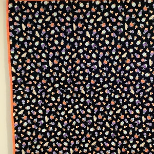 K&ouml;nnte beinhalten: Eine schwarze Steppdecke mit einem sich wiederholenden Muster von Halloween-S&uuml;&szlig;igkeiten, Cupcakes und Lollis in Orange, Lila und Wei&szlig;. Die Steppdecke hat einen orangefarbenen Rand und h&auml;ngt an Gardinenringen.