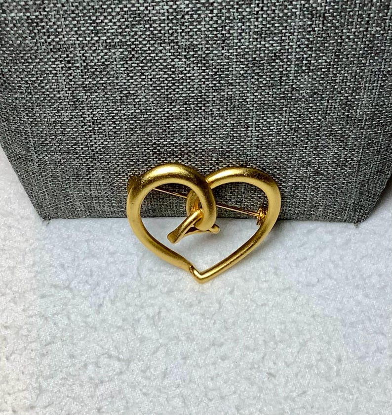 May include: A gold-toned heart-shaped brooch with a knotted design in the center.