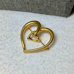 May include: A gold-toned heart-shaped brooch with a smaller heart intertwined within the larger heart.