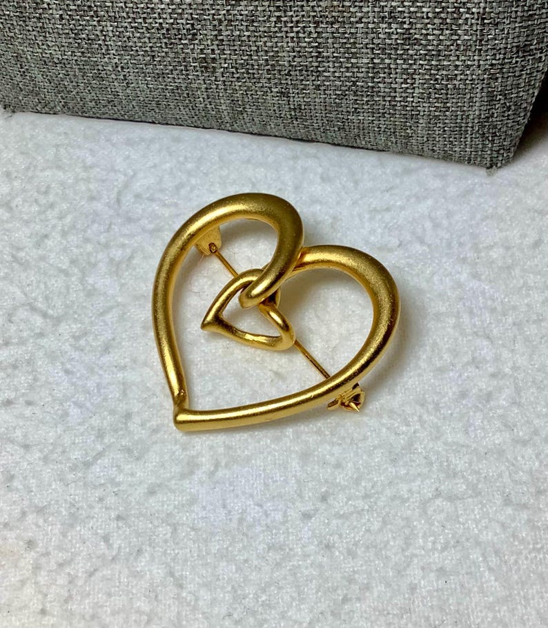 May include: A gold-toned heart-shaped brooch with a smaller heart intertwined within the larger heart.