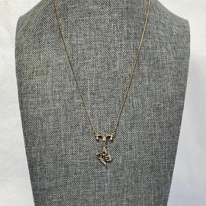 以下が含まれることがあります： 蝶のペンダントが付いたゴールドトーンのネックレス。ペンダントは、黒のアクセントと小さな透明な石を備えた詳細な蝶のデザインが特徴です。 ネックレスは灰色のマネキンに表示されています。