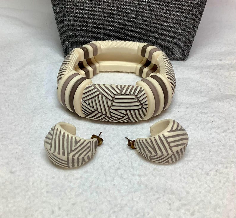 May include: A cream-colored bracelet and matching hoop earrings set. The bracelet features alternating cream and brown segments with a geometric design. The earrings have a similar pattern. The jewelry set is displayed on a white surface.