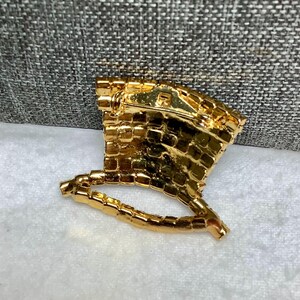 May include: Gold-toned brooch shaped like a hat with a rhinestone design. The brooch has a pin back.