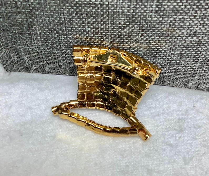 May include: Gold-toned brooch shaped like a hat with a rhinestone design. The brooch has a pin back.