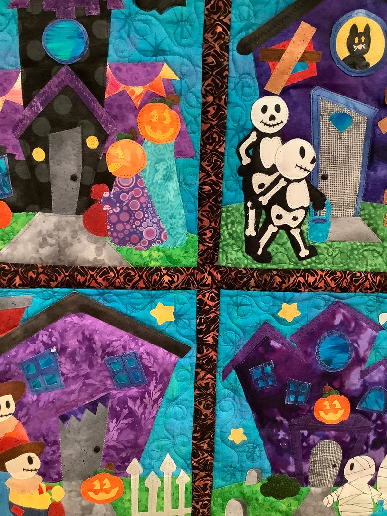 K&ouml;nnte beinhalten: Eine gesteppte Halloween-Wanddekoration mit skurrilen H&auml;usern, K&uuml;rbissen und Skelettfiguren. Die H&auml;user sind lila und schwarz mit verschiedenen Details. Der Hintergrund ist hellblau mit Stern- und Bl&auml;ttermustern.