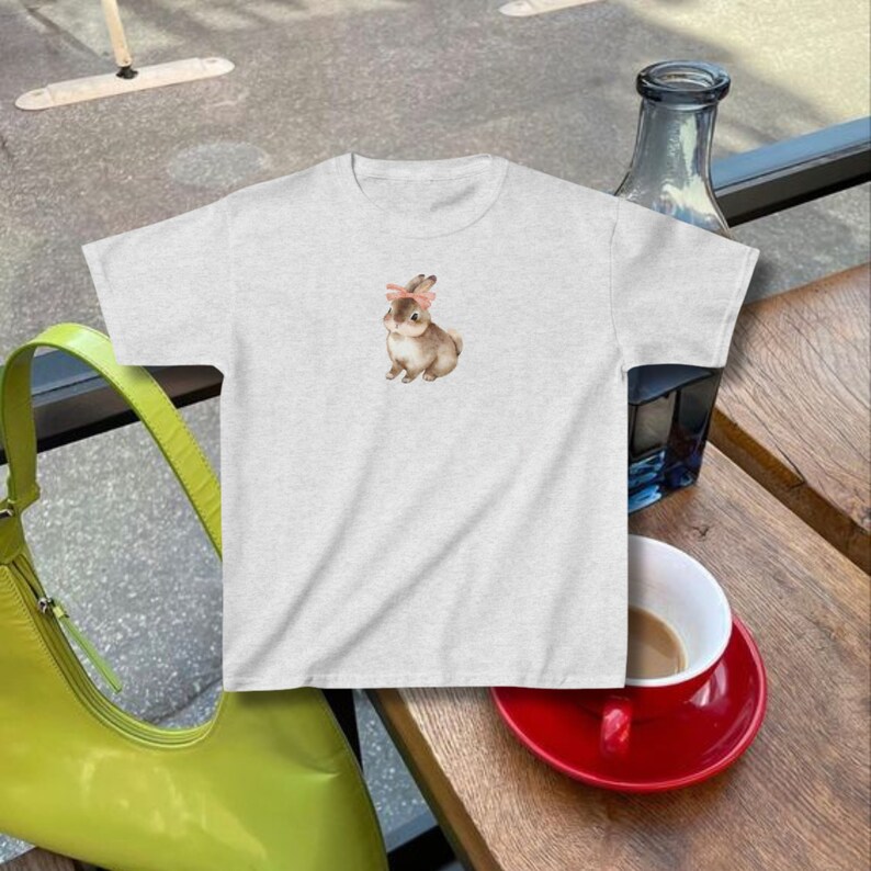 model wears a fitted crop top baby tee with a bunny rabbit on it wearing a pink ribbon bow in the style of coquette cottagecore downtown girl clean girl aesthetic