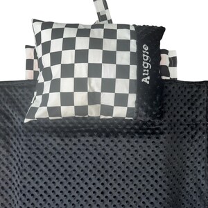 May include: Black and white checkered pillow with the name "Auggie" embroidered on it. The pillow is sitting on a black, textured blanket.