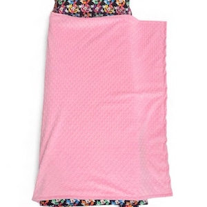 May include: A pink nap mat set with a patterned pillow and footrest. The pillow and footrest feature a colorful repeating pattern of cartoon characters on a black background. The blanket is a solid pink color.