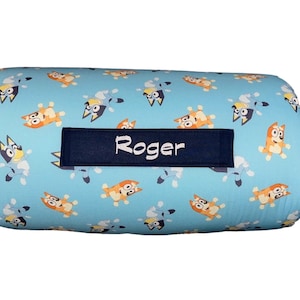 May include: A blue and white patterned cylindrical pillow with a navy blue label that says "Roger".