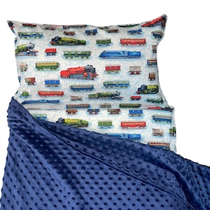 May include: A blue fleece blanket with a train pattern pillow on top. The pillow is white with a blue and red train pattern.