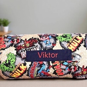 May include: A cylindrical bolster pillow featuring a colorful Marvel comic book print with characters like Hulk, Iron Man, Thor, and Spider-Man. A dark blue rectangular fabric patch is centered on the front with the name Viktor in red text.