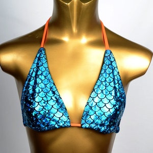May include: A blue bikini top with a scale pattern, displayed on a gold mannequin. The bikini has orange straps and a triangle shape. The scale pattern has a shimmering effect.