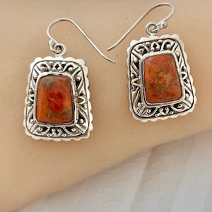 May include: A pair of silver earrings with orange stone accents. The earrings have a detailed filigree design and feature a rectangular stone.