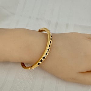 May include: A gold bangle bracelet with a row of black and white rhinestones.