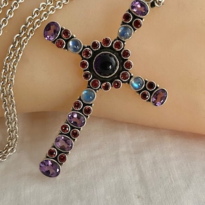 May include: A silver chain necklace with a cross pendant featuring a variety of gemstones, including amethyst, moonstone, and garnet.